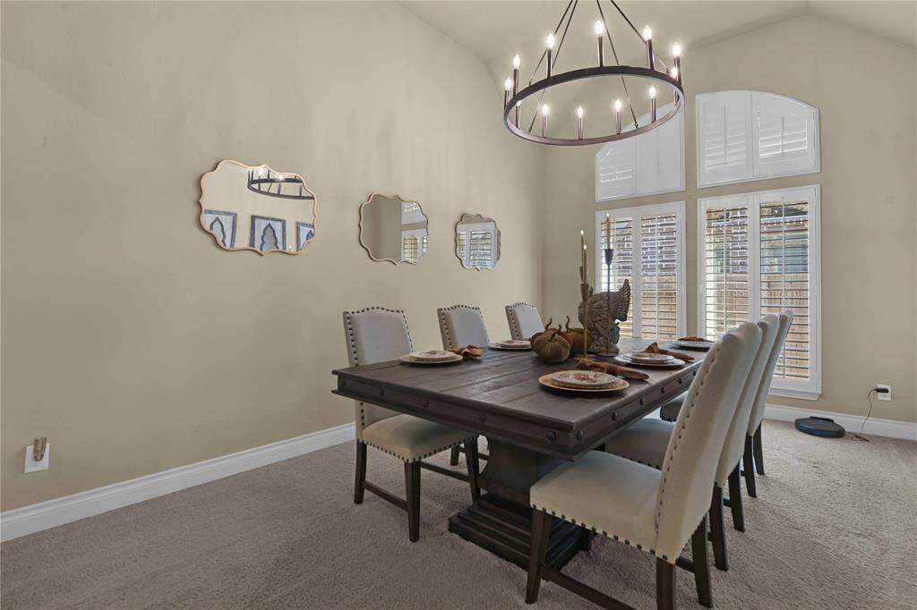 The oversized formal dining room provides ample space for hosting elegant dinners, featuring a high vaulted ceiling adorned with a unique farmhouse-style chandelier. Plush carpet underfoot adds a touch of comfort, while large windows with plantation shutters enhance the room’s elegance and allow for plenty of natural light
