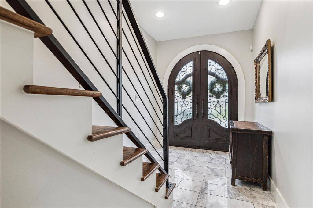 An elegant entry way with double arched front doors, white tile flooring, and high ceilings provide and warm entrance.