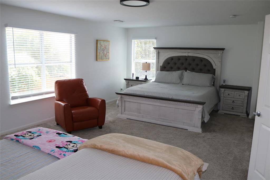 The well-lit primary bedroom features large windows, plush carpeting and neutral color tones offering a serene  and cozy atmosphere.