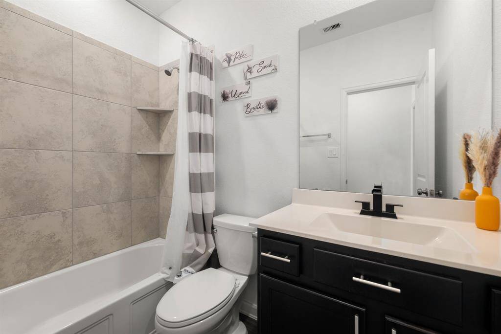 Secondary bathroom features light countertops and dark cabinets, neutral paint, shower/tub combo with tile surround, large mirror, tile floors, sleek fixtures and modern finishes with plenty of space to accommodate any visiting family or guests.
