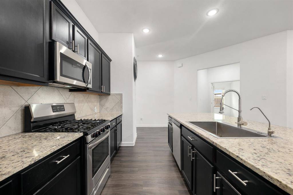 This stunning kitchen displays such a beautiful contrast with the dark cabinets, custom neutral paint, granite countertops, light modern backsplash, and SS appliances, oversized kitchen island with extra storage, breakfast bar, recessed lighting, high ceilings and pantry.