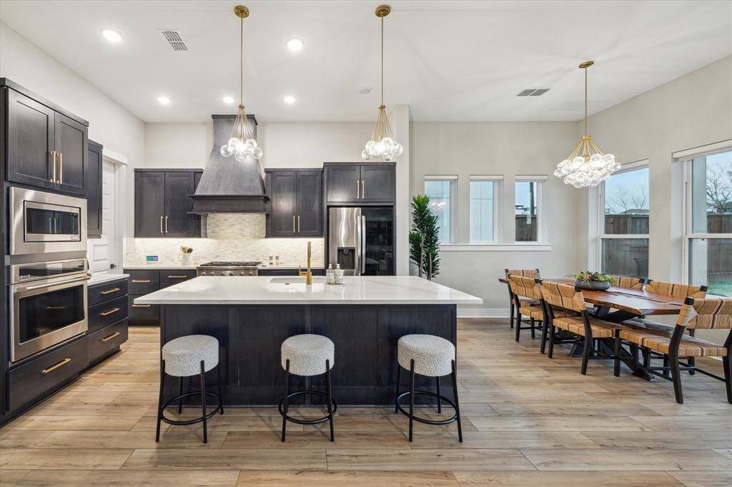 Stainless steel appliances complement dark cabinets and gold hardware beautifully, adding a sleek, modern touch while balancing warmth and depth.