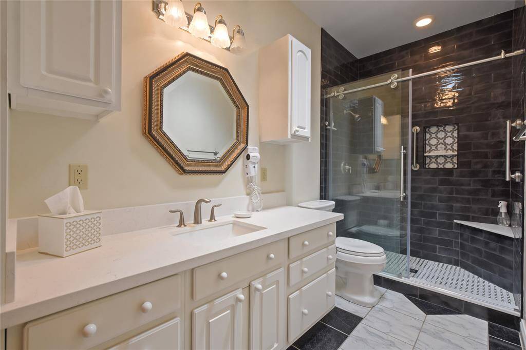 The renovated hall bath features revised tile flooring and a large shower area with glass door and revised fixtures and hardware.