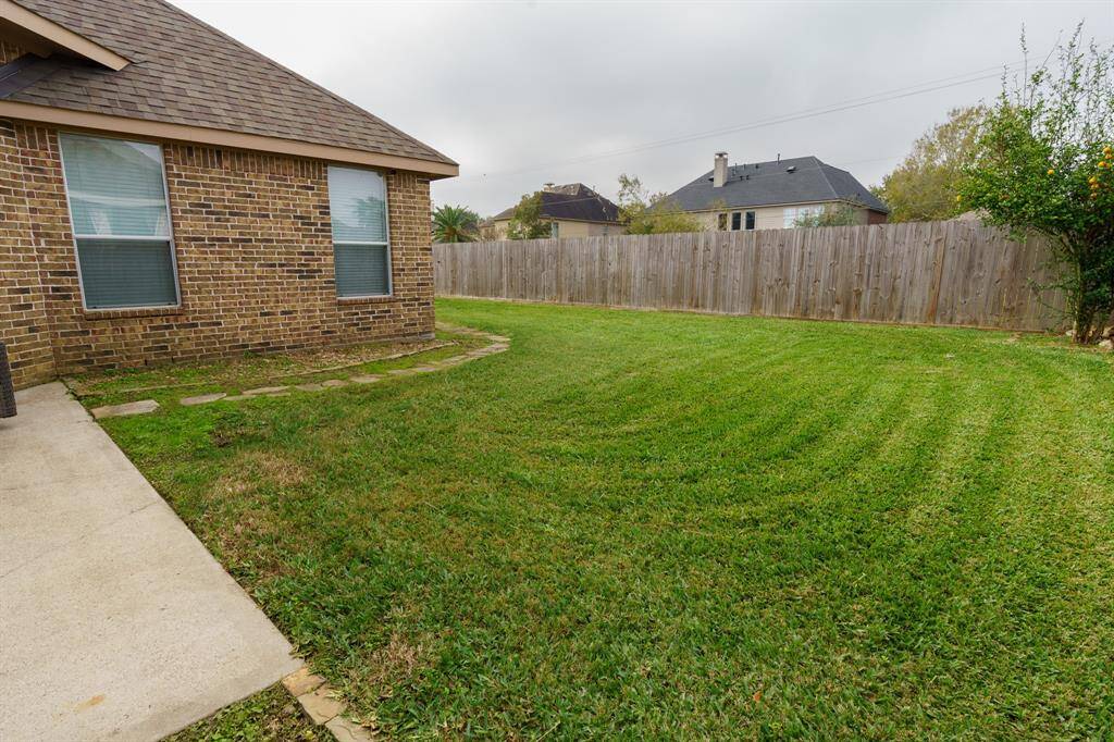 A spacious backyard with a well-maintained lawn, featuring a brick exterior, a small patio area with seating, and a storage shed, all enclosed by a wooden fence for privacy.