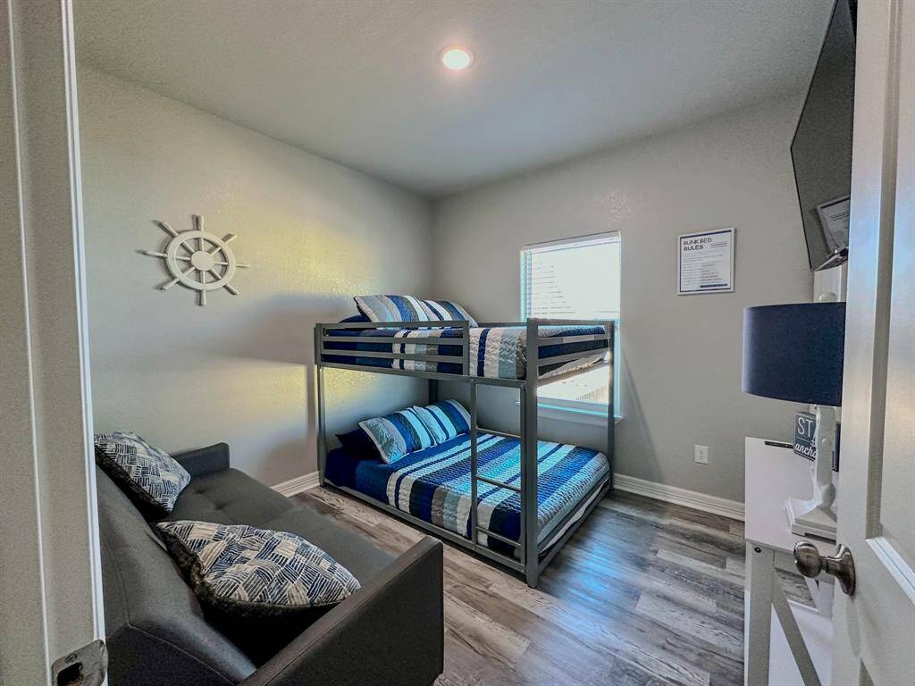 This bedroom with ensuite features a bunk bed with nautical-themed bedding, a small window, and a wall-mounted TV. The room has wood-style flooring and soft lighting.