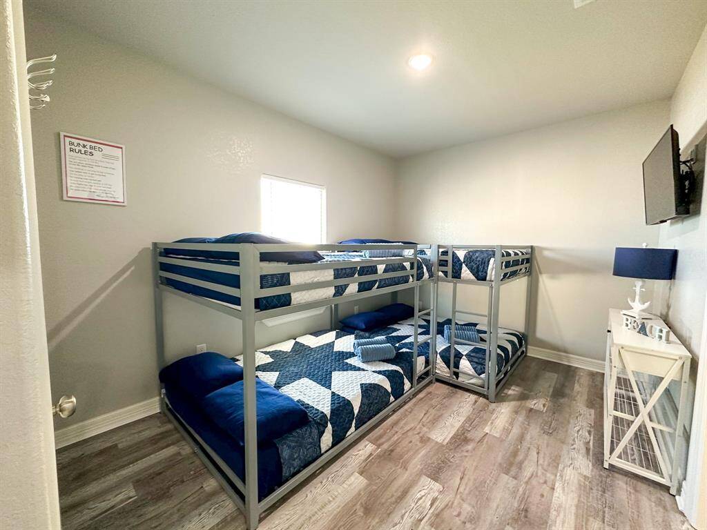 This bedroom features two sets of bunk beds, perfect for accommodating multiple guests or children. It has light walls, wood-look flooring, and a window for natural light. A dresser with a lamp and decor adds a welcoming touch.