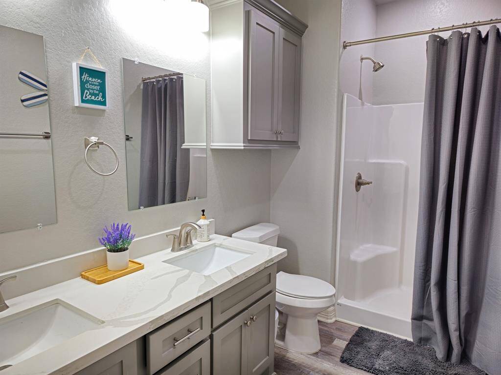 The 2ns ensuite bathroom features a modern design with a double vanity, sleek gray cabinets, and a spacious walk-in shower with a curtain. The neutral color palette is complemented by stylish fixtures and decorative touches, creating a clean and inviting space.