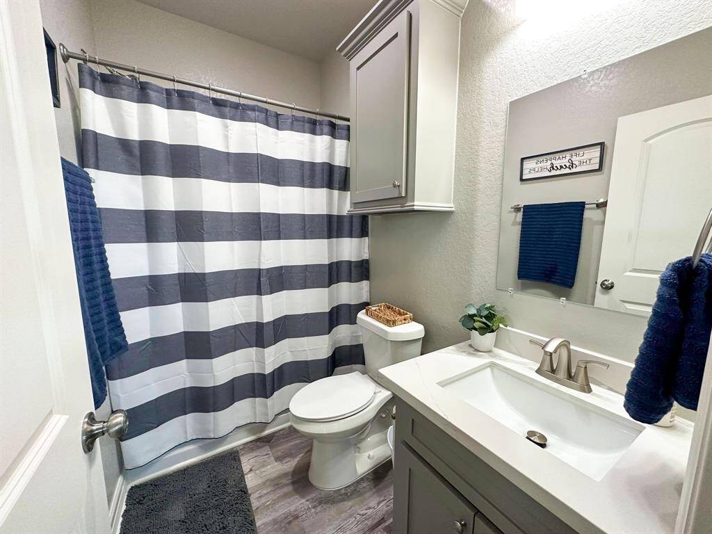 This is a modern guest bathroom featuring a sleek design with a striped shower curtain, a white vanity with ample storage, and contemporary fixtures. The space is accented with blue towels and a small plant, creating a fresh and inviting atmosphere.