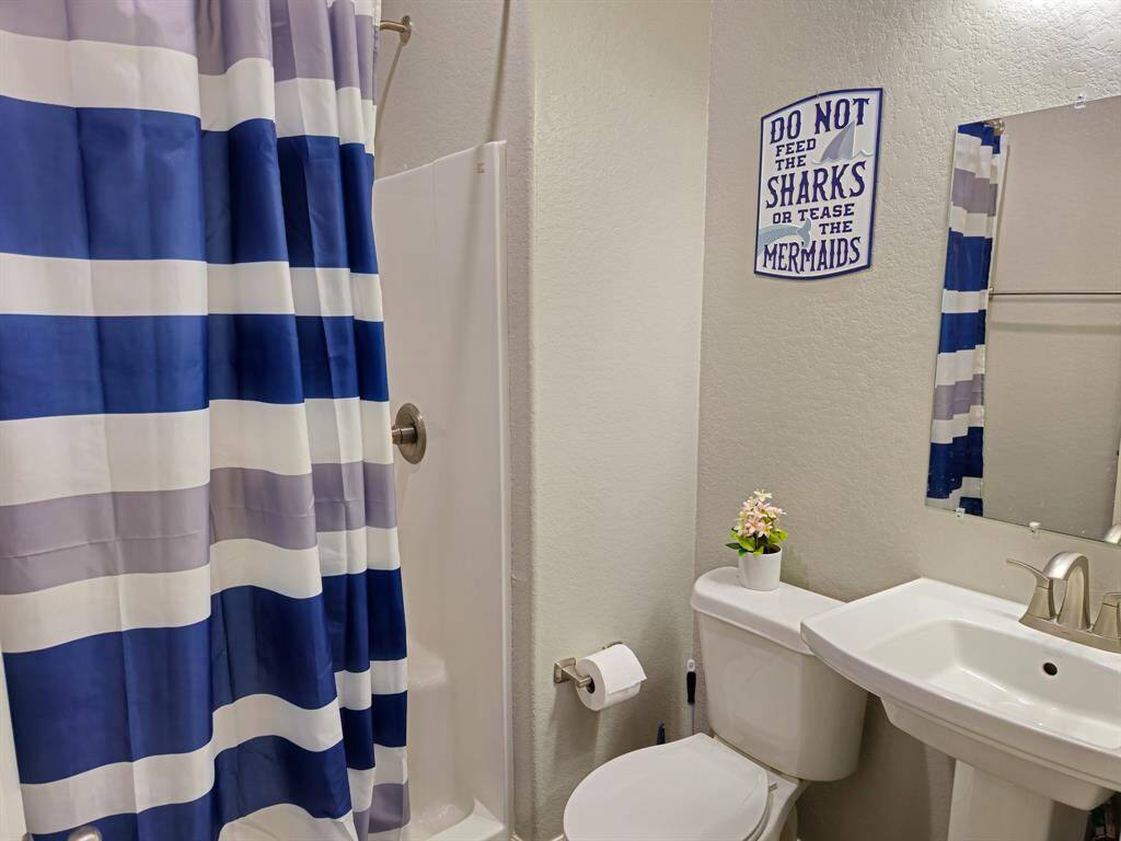 The 3rd ensuite bath, featuring a modern pedestal sink, and shower with a blue and white striped curtain. The decor includes a playful wall sign and a small plant for a touch of charm.