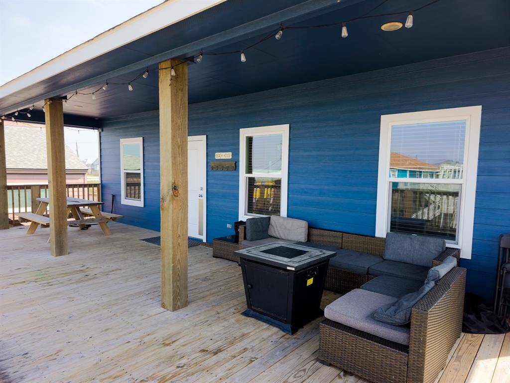 This photo showcases a spacious wooden deck with a cozy outdoor seating area and a picnic table. The blue exterior wall adds a vibrant touch, and there are overhead string lights for evening ambiance. Perfect for relaxing or entertaining outdoors.