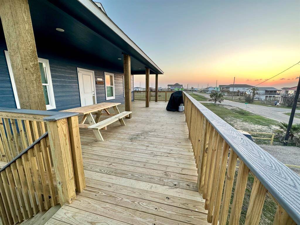 This photo shows a spacious wooden deck, featuring a picnic table and grill. The deck offers a view of a quiet neighborhood street and a beautiful bay sunset, creating a perfect space for outdoor relaxation and entertaining.