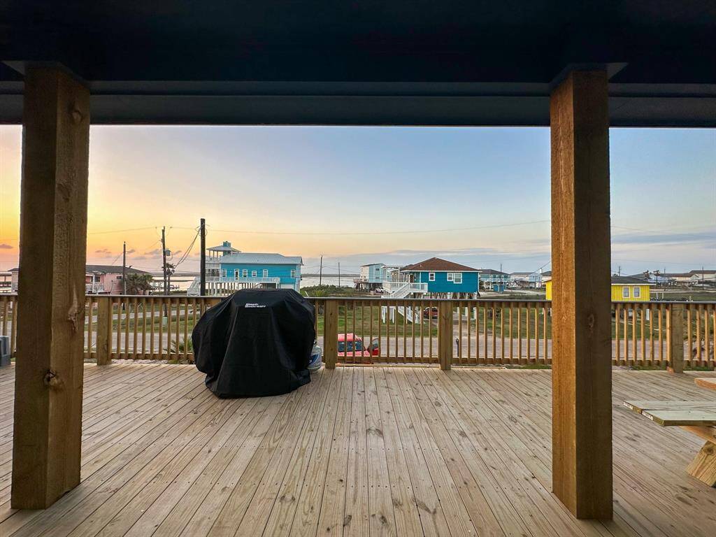 Spacious wooden deck with sunset bay views, perfect for outdoor relaxation. Features a railing and BBQ setup, offering a cozy spot for gatherings with a picturesque sunset backdrop.