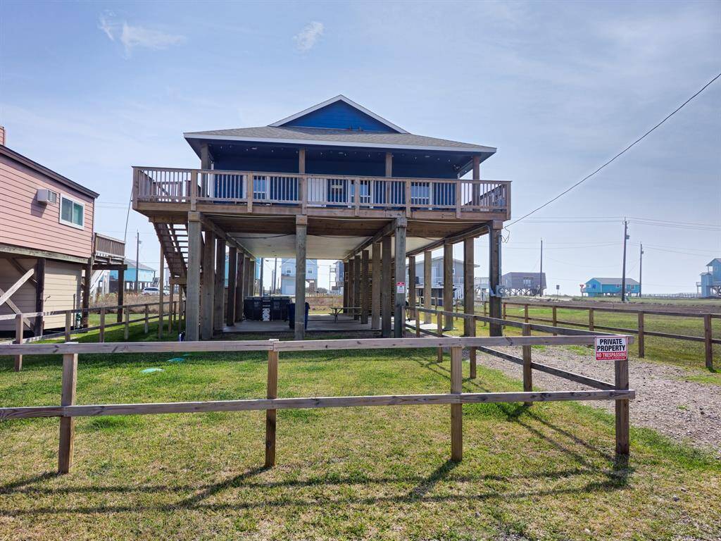 Elevated beach house with a spacious wraparound deck, set on stilts for flood protection. The property includes a fenced yard and offers ample space underneath for parking, storage, entertaining and ideal for coastal living.