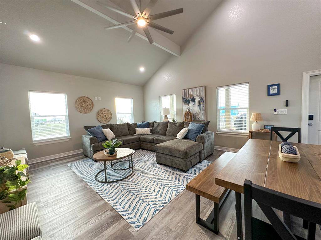 This inviting living room features high ceilings with a ceiling fan, large windows for natural light, and stylish decor. It includes a comfortable sectional sofa, a cozy rug, and a dining table, creating a perfect space for relaxation and entertaining.