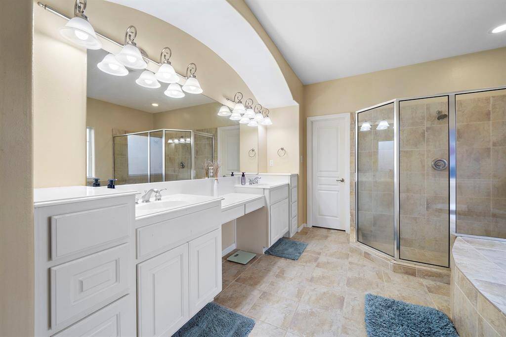 Indulge in the luxurious primary bathroom featuring double sinks, a jetted tub, a walk-in shower, a vanity, a linen closet, and easy access to the walk-in closet.