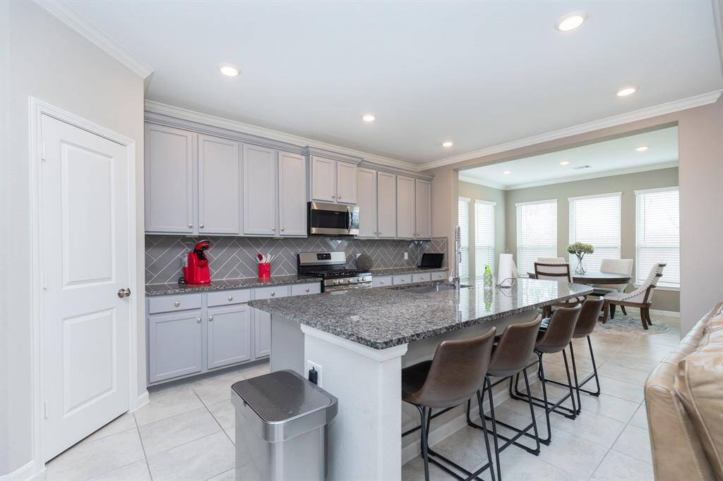 kitchen features gray cabinetry, a large granite island with seating, stainless steel appliances, and an open layout that flows into a breakfast area.