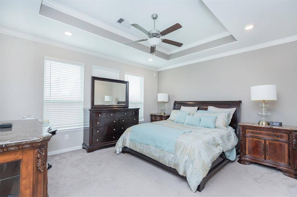 Spacious bedroom with a tray ceiling, featuring a ceiling fan and recessed lighting.