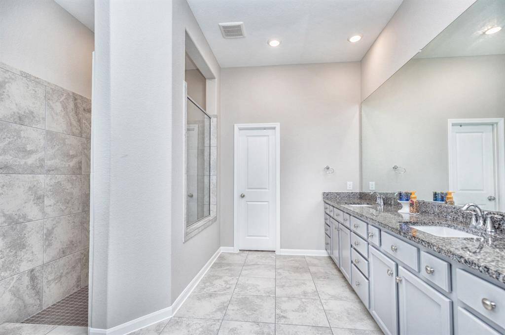 bathroom features a spacious layout with a large walk-in shower, dual sink vanity with granite countertops, ample storage, and elegant tile flooring.