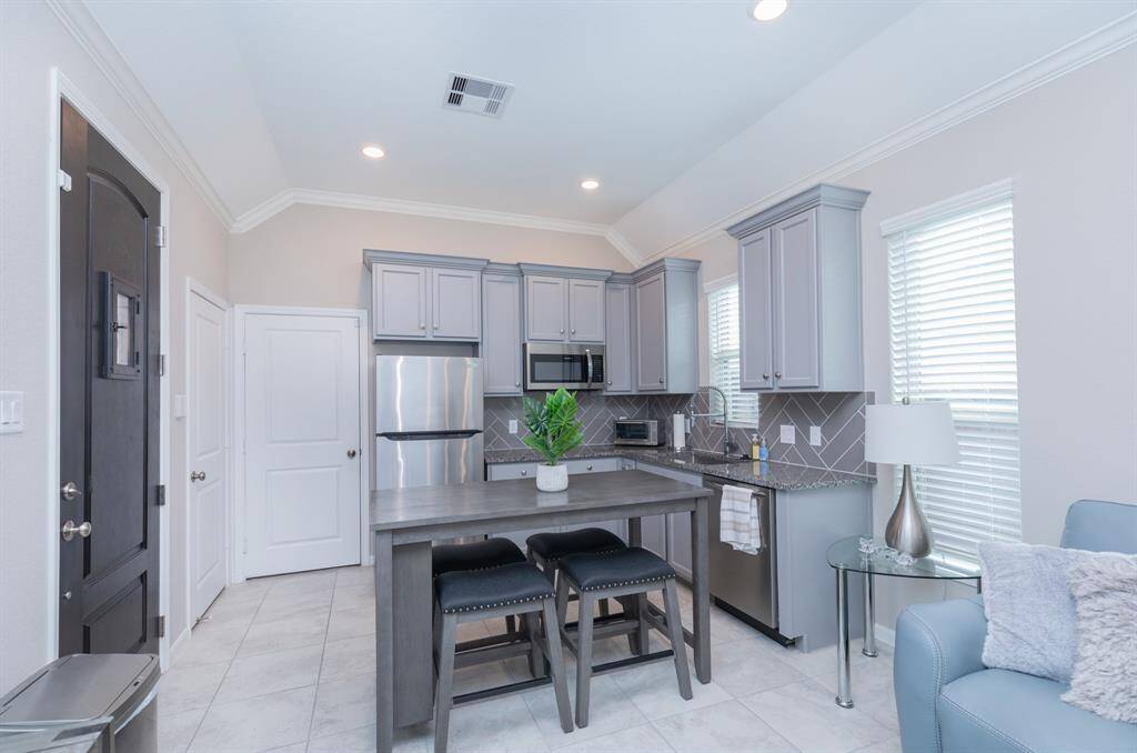 This modern kitchen features sleek gray cabinetry, stainless steel appliances, and a stylish island with seating. The room is brightened by ample natural light from large windows and complemented by contemporary decor.