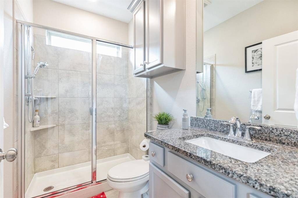 This photo showcases the Next Gen suite bathroom, designed with sleek, modern finishes. It includes a glass-enclosed shower, a beautiful granite countertop, and contemporary fixtures. The neutral tones and abundant lighting enhance the space, creating a bright, airy, and inviting atmosphere.