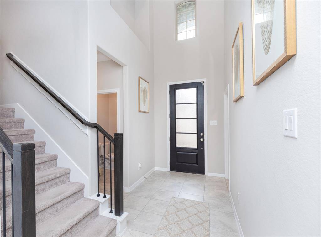 welcoming entryway with high ceilings, a modern black front door with frosted glass, and light tiled flooring.