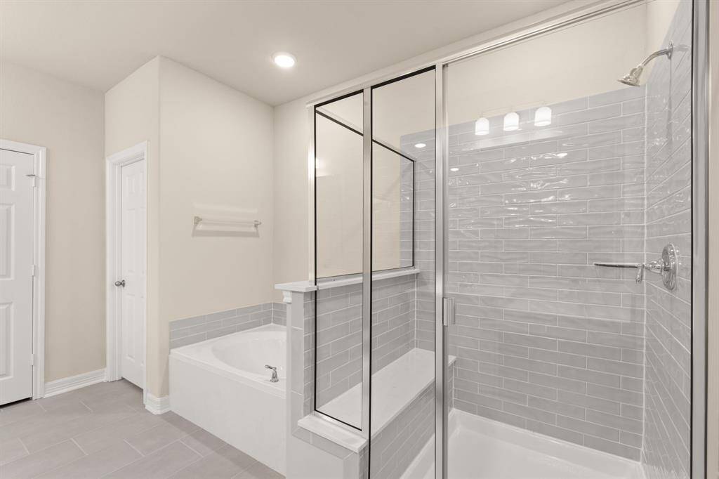 This additional view of your primary bathroom features tile flooring, fresh paint, walk-in shower, a separate garden tub, and a large walk-in closet.
