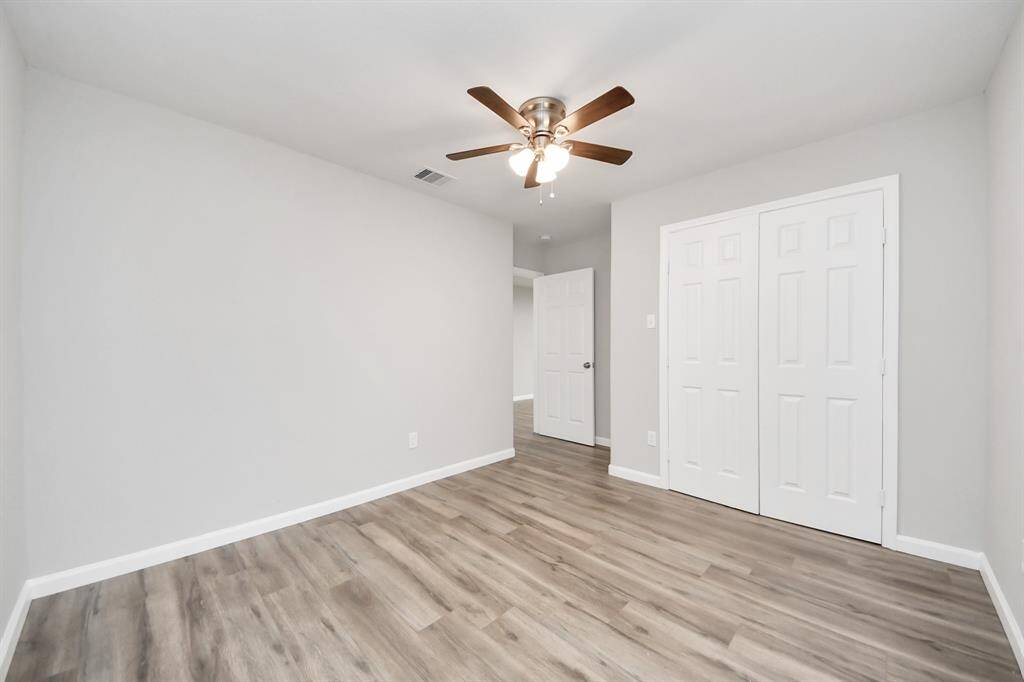 This room features fresh gray walls, laminate wood flooring, and a ceiling fan. It offers a spacious feel with a double-door closet, ideal for a bedroom or office space.