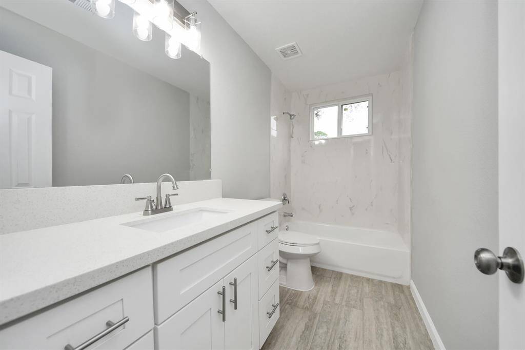 This bathroom features a modern, clean design with a spacious white vanity, sleek fixtures, and a bathtub. The room is bright and airy, complemented by light wood-look flooring and a large mirror with contemporary lighting.