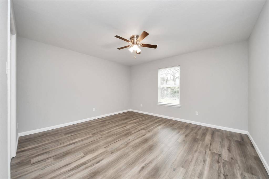This room features a modern look with light gray walls, laminate wood flooring, and a ceiling fan. A large window provides natural light, creating a bright and airy atmosphere.