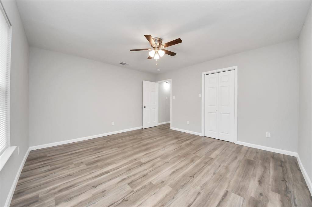 This room features fresh, neutral paint, laminate wood flooring, a ceiling fan, and a closet with double doors. It's bright and spacious, ideal for a bedroom or home office.