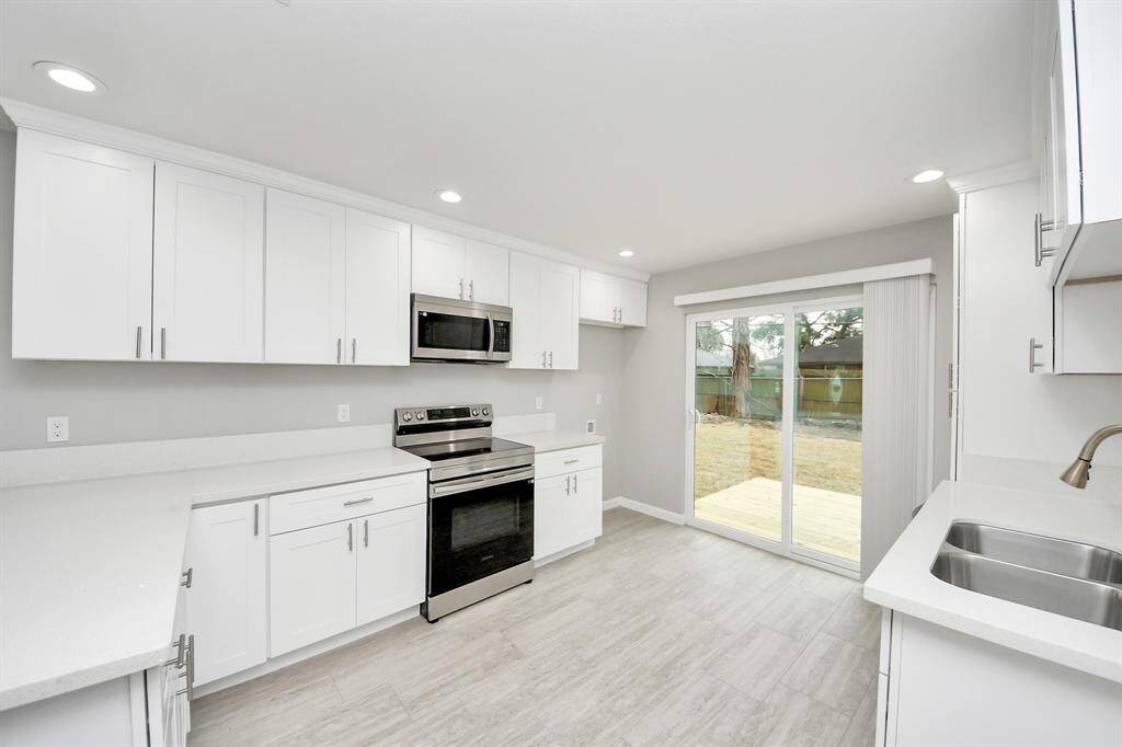 This modern kitchen features sleek white cabinetry, stainless steel appliances, and ample counter space. It opens up to a backyard through large sliding glass doors, allowing plenty of natural light.