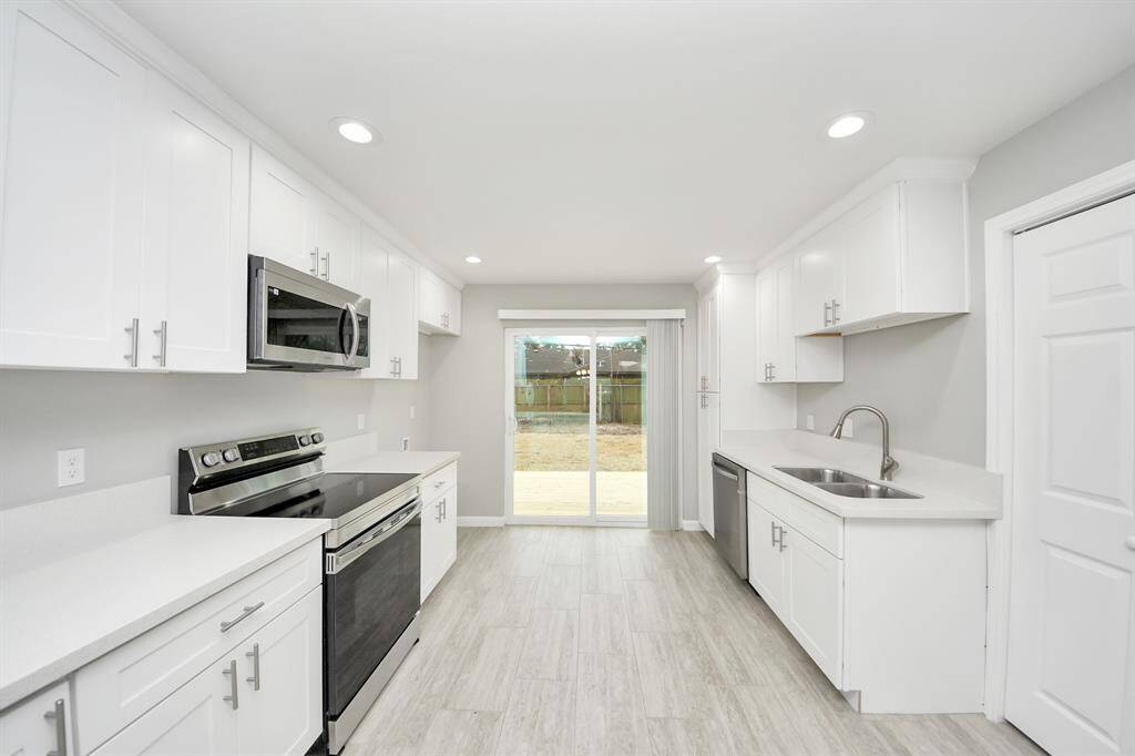 Modern kitchen with sleek white cabinetry, stainless steel appliances, and ample counter space. The room is brightened by recessed lighting and features a sliding glass door leading to the backyard, enhancing the open feel.