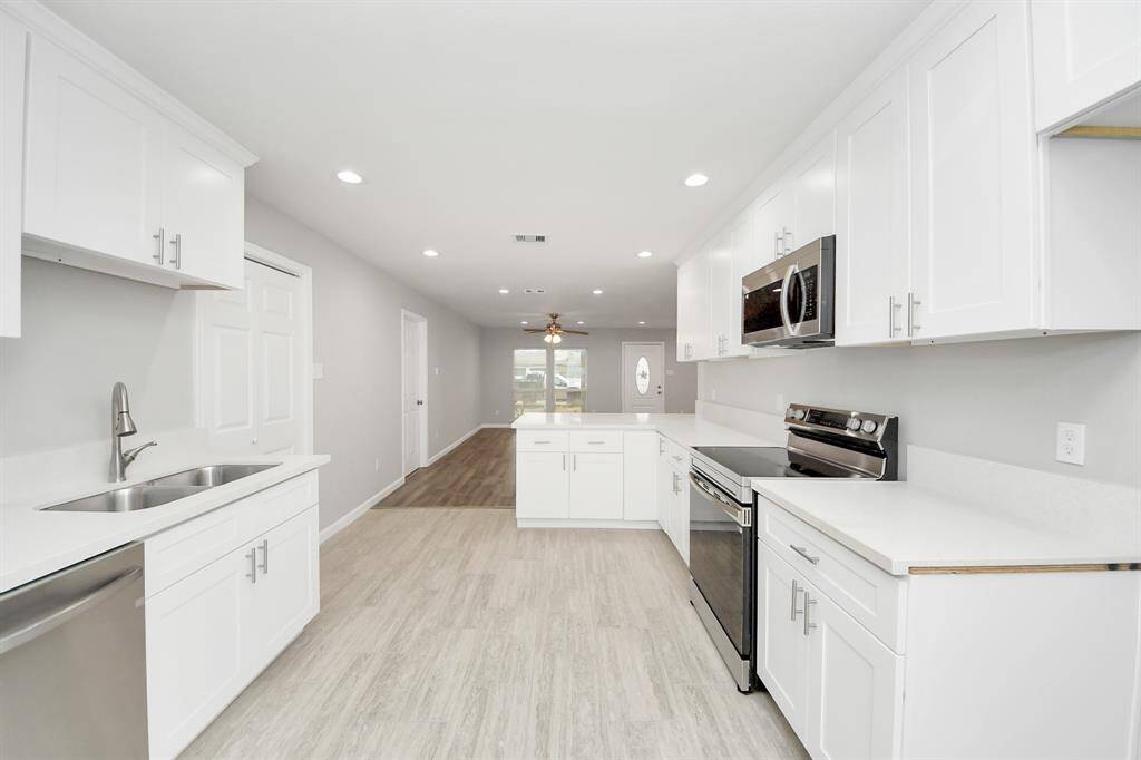 This kitchen features a modern, open design with white cabinetry, stainless steel appliances, and light wood flooring. The space is bright with recessed lighting and has ample counter space for cooking and entertaining.