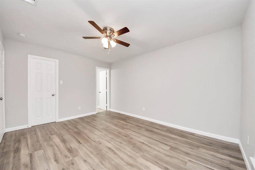 This room features neutral walls, laminate wood-style flooring, and a ceiling fan. It's bright and open, with two doors leading to other areas, offering versatility for various uses.
