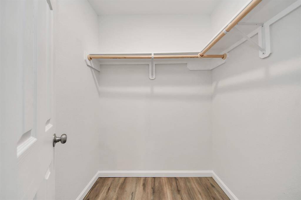 This is a spacious walk-in closet with white walls, wooden rod hangers, and a laminate wood floor, providing ample storage space.