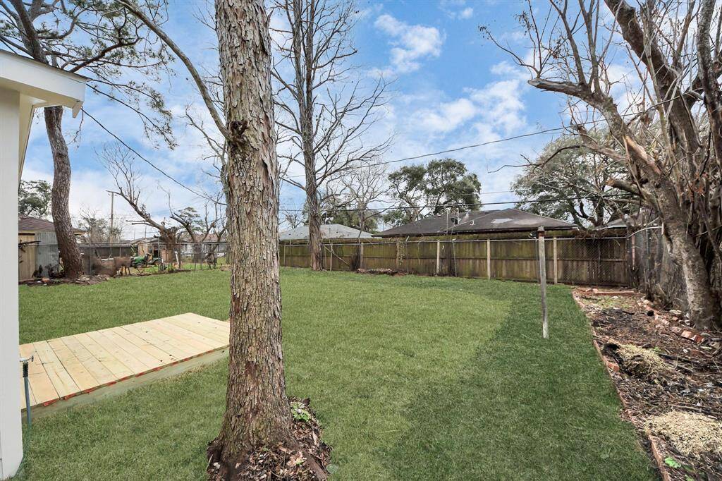 Spacious backyard with a lush green lawn, mature trees, and a wooden deck, ideal for outdoor activities and relaxation.