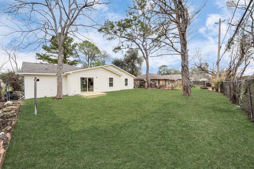 This photo shows a spacious backyard with a lush green lawn and mature trees, featuring a single-story white house with sliding glass doors opening to the yard. Ideal for outdoor activities and entertaining.