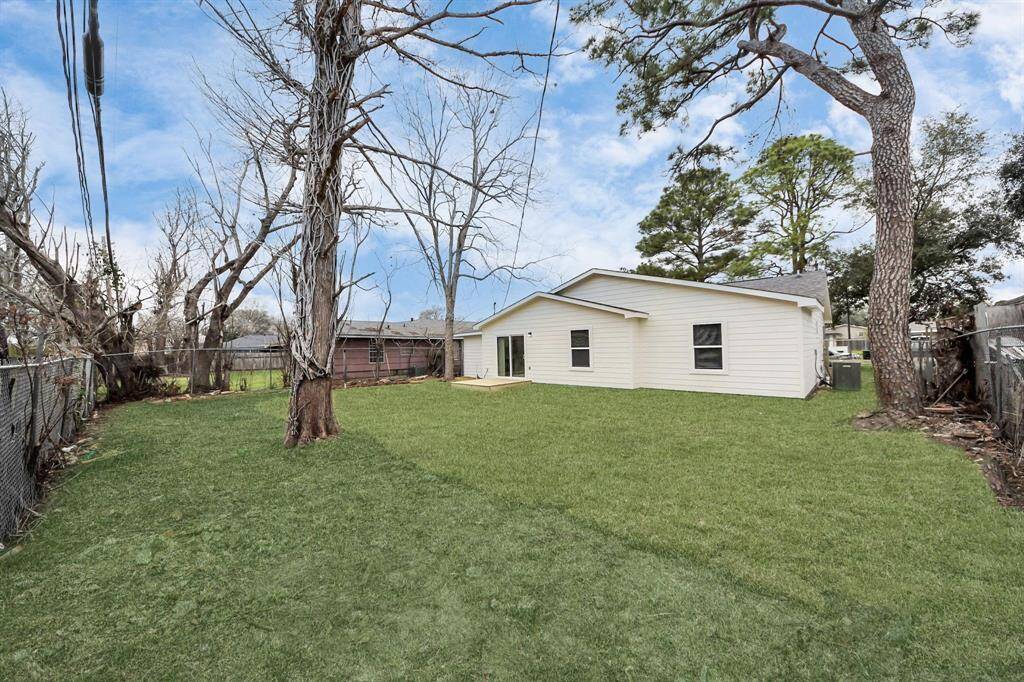 Spacious backyard with a well-maintained lawn, mature trees, and a fenced perimeter, providing privacy and ample outdoor space. The house features a light exterior with multiple windows for natural light.