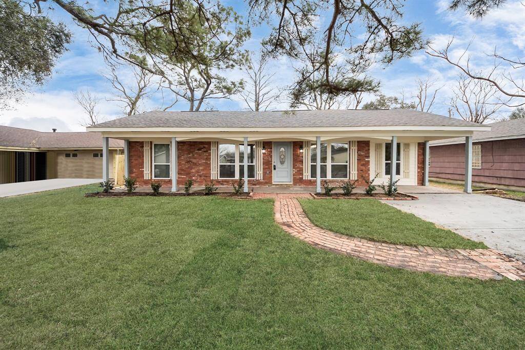 This charming single-story home features a classic red brick exterior with a welcoming front porch and a traditional gable roof. The well-maintained front yard includes a quaint brick pathway and mature trees, providing great curb appeal.