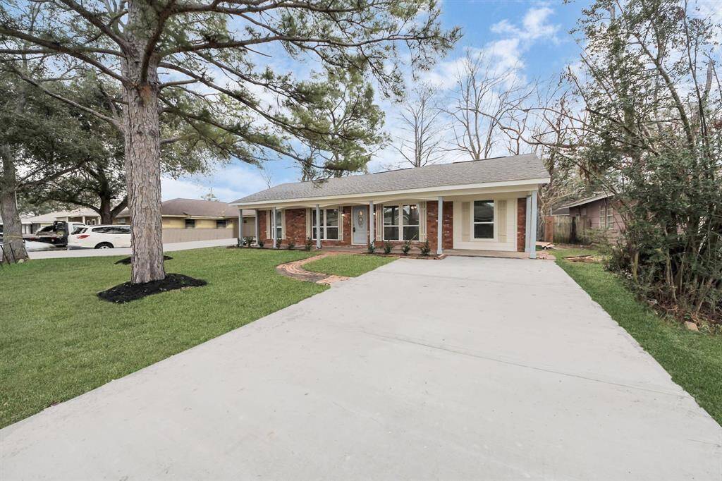 Charming single-story home with a classic brick facade and inviting front porch. The spacious driveway leads to a well-maintained lawn surrounded by mature trees, offering a serene and welcoming atmosphere.
