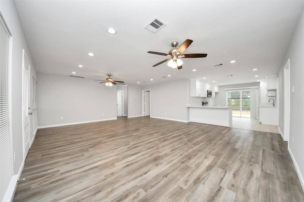 This spacious open-concept living area features stylish laminate wood flooring, ceiling fans, and recessed lighting. The modern kitchen with a breakfast bar seamlessly connects to the living space, and large sliding glass doors provide natural light and access to the backyard.