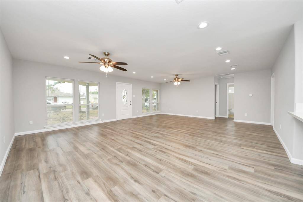 This photo showcases a spacious, open-concept living area with laminate wood flooring, neutral walls, and ample natural light from multiple windows. It features modern ceiling fans and recessed lighting, creating a bright and inviting atmosphere.