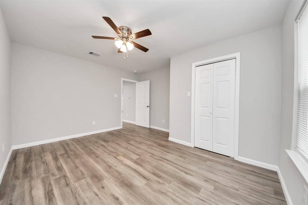 This room features modern laminate flooring and soft gray walls, creating a bright, inviting space. It includes a ceiling fan, a window for natural light, and a closet with white double doors, perfect for storage.
