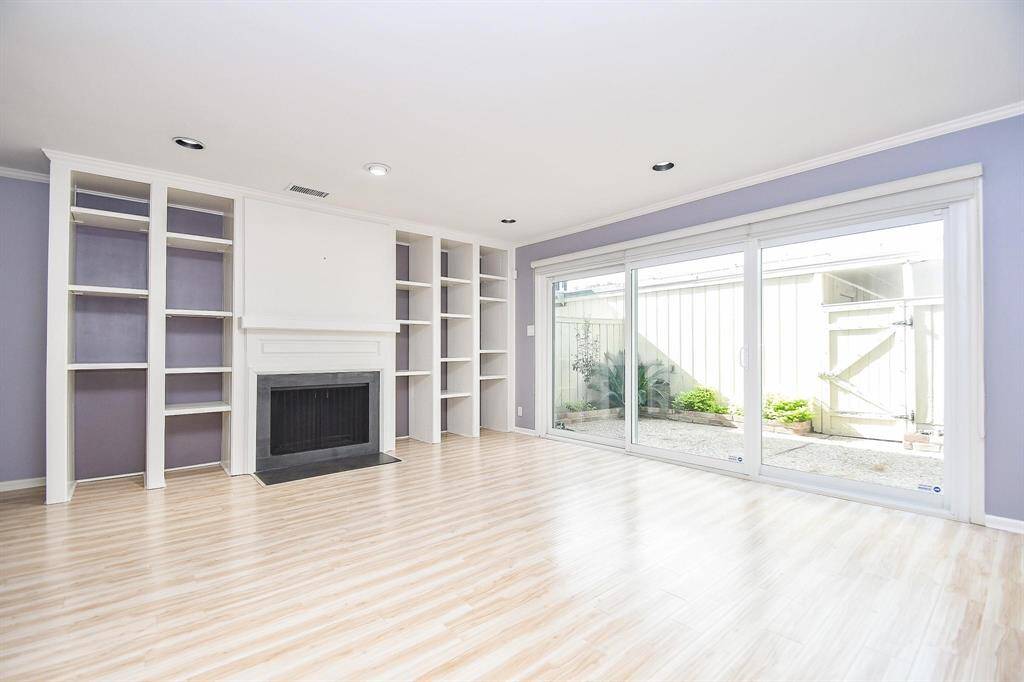 This bright living room features built-in shelving around a central fireplace, and large sliding glass doors that open to an outdoor area, providing ample natural light.