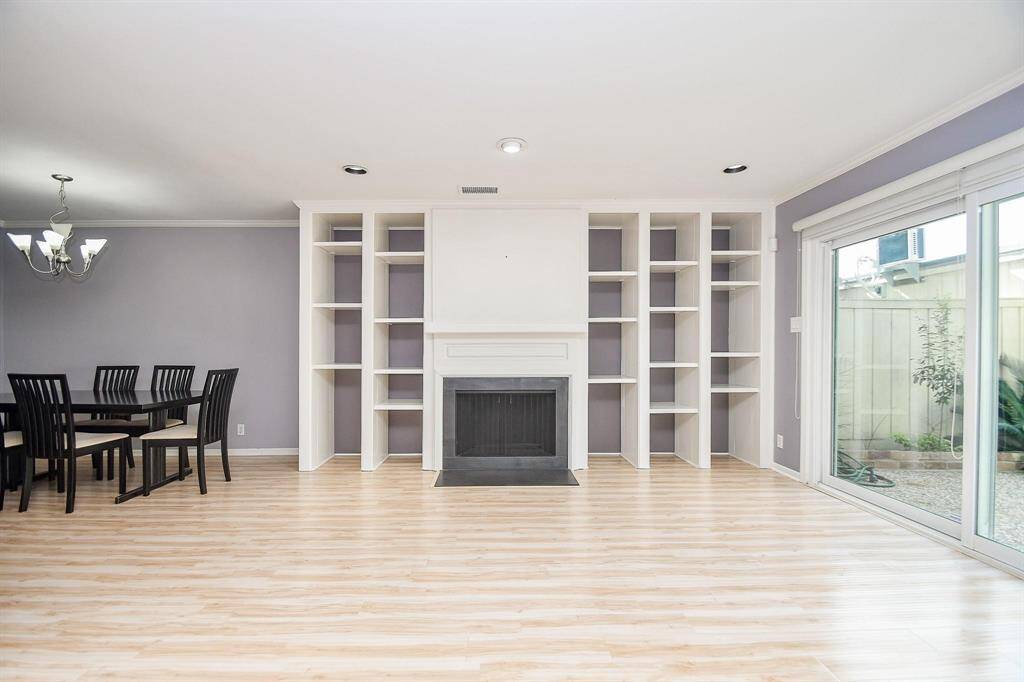 This spacious, bright room features laminate wood flooring, built-in shelves surrounding a central fireplace, and large sliding glass doors leading outside.