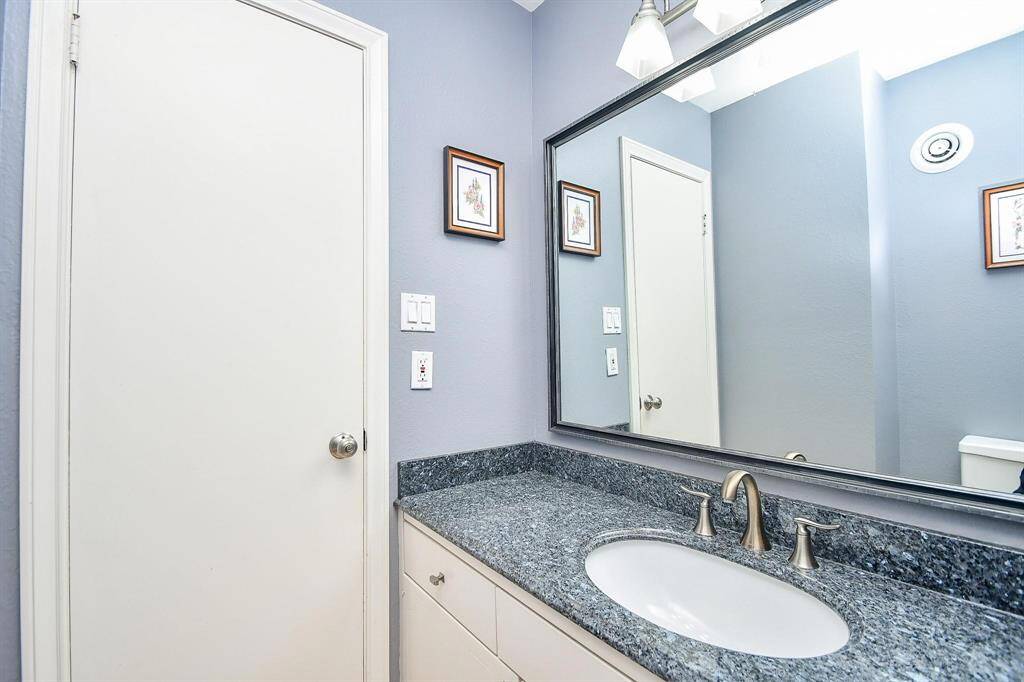 This bathroom features a sleek granite countertop with an under-mount sink, a large mirror, soft blue walls, and modern fixtures, creating a clean and contemporary look.
