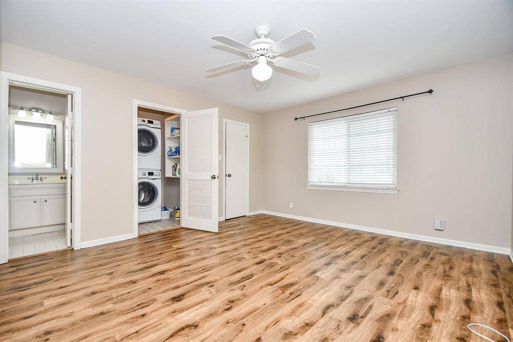 This bright room features vinyl wood flooring, a ceiling fan, and large window. It includes an adjacent bathroom and a convenient laundry area with almost new stackable washer and dryer. Ideal for a cozy living space or bedroom setup.