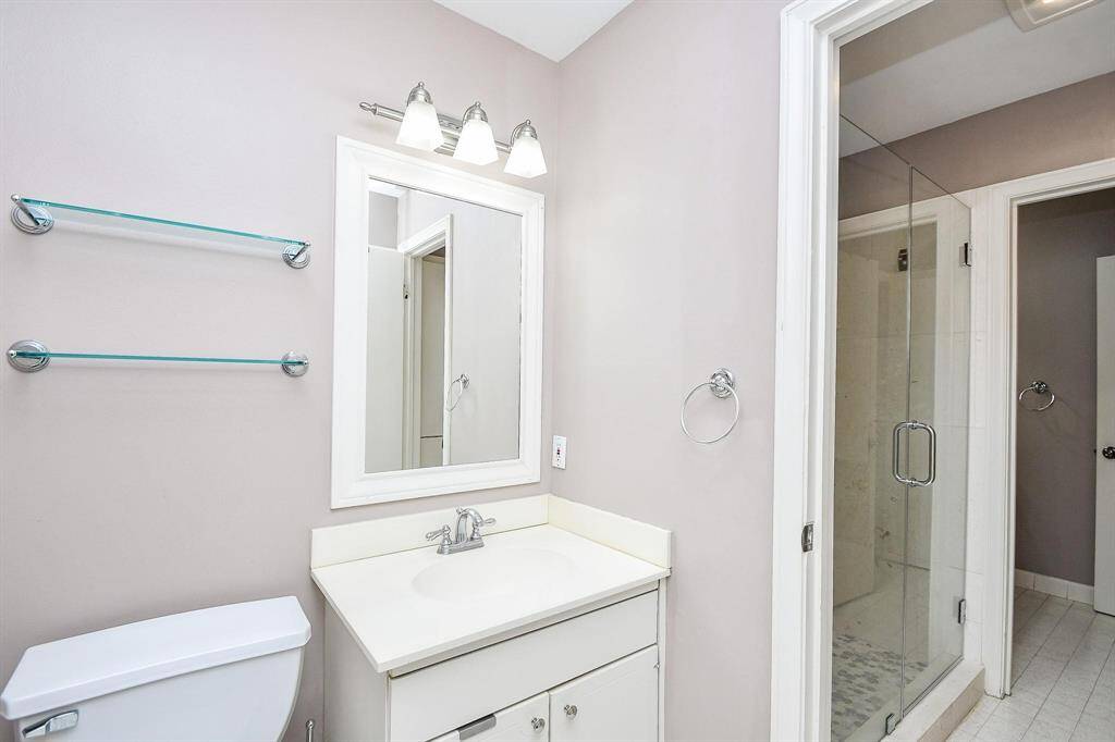 This bathroom features a modern design with a glass-enclosed shower, white vanity with a mirror, and sleek fixtures. The neutral color palette adds a clean and spacious feel.
