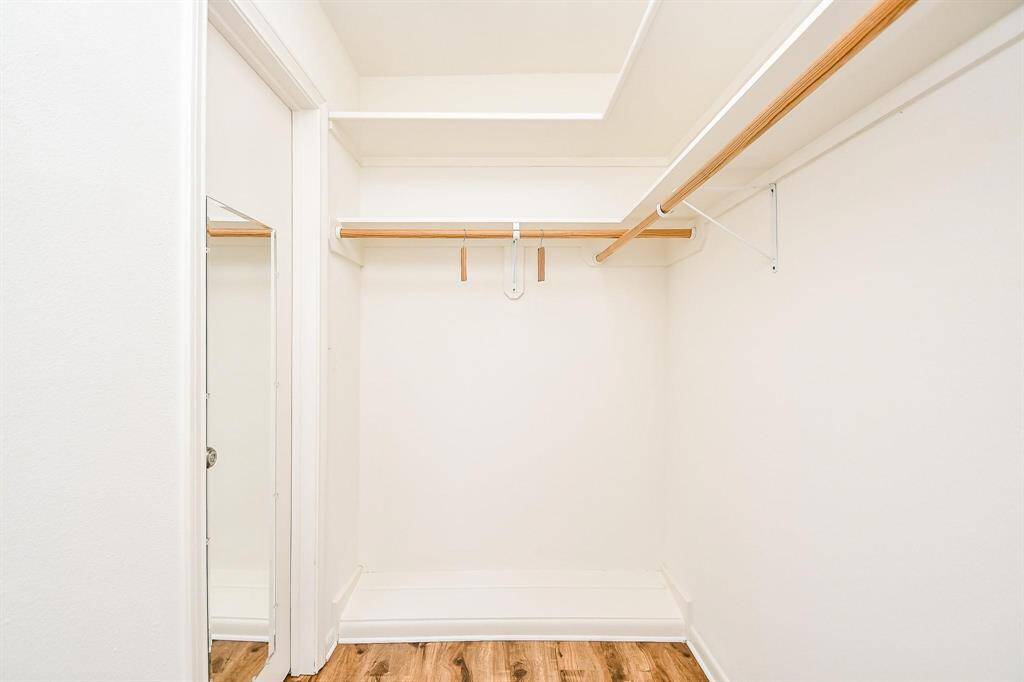 This photo shows a spacious walk-in closet with white walls, wooden hanging rods, and light wood flooring, offering ample storage space.