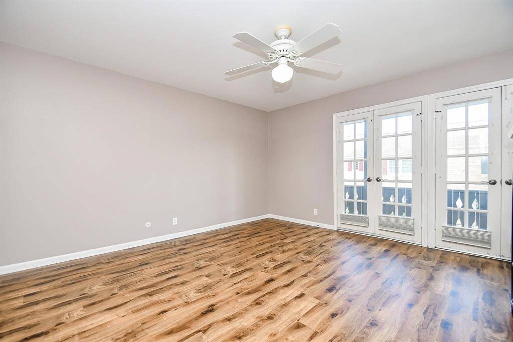 The bedroom features wood flooring, neutral walls, a ceiling fan, and double French doors leading to a balcony, offering a bright and airy space.